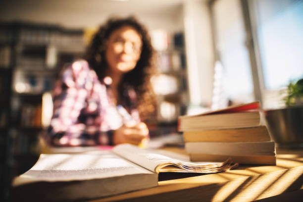 istock Close up view of book stack on the table and young brunette studying in the background. 941258800