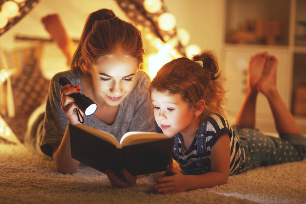 istock mother and child daughter reading a book and a flashlight before going to bed 941259114