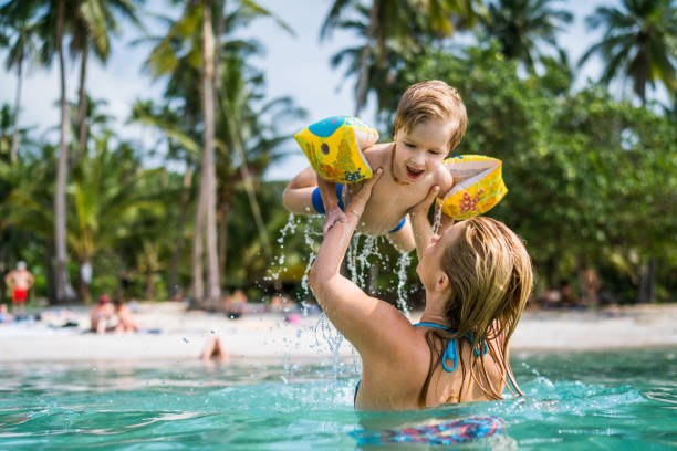 niño feliz divertirse en el mar mientras que siendo sostenido por su madre. - family beach vacations travel fotografías e imágenes de stock