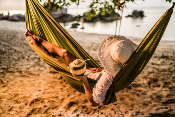 donna con bevanda al cocco rilassante sull'amaca in spiaggia. - hammock beach vacations tropical climate foto e immagini stock