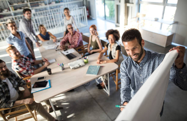 Above view of happy entrepreneur explaining the business plan to his team on a presentation in the office. High angle view of happy businessman writing a business plan on whiteboard during a presentation in the office. creative writing class stock pictures, royalty-free photos & images