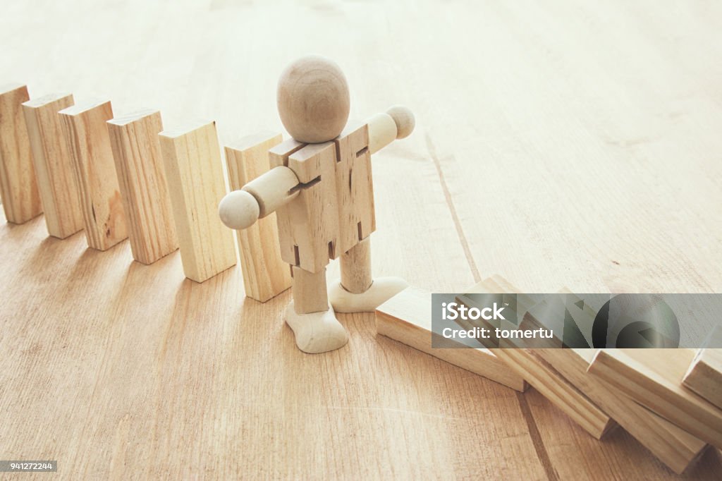 A wooden dummy stopping the domino effect. retro style image executive and risk control concept. A wooden dummy stopping the domino effect. retro style image executive and risk control concept Business Stock Photo