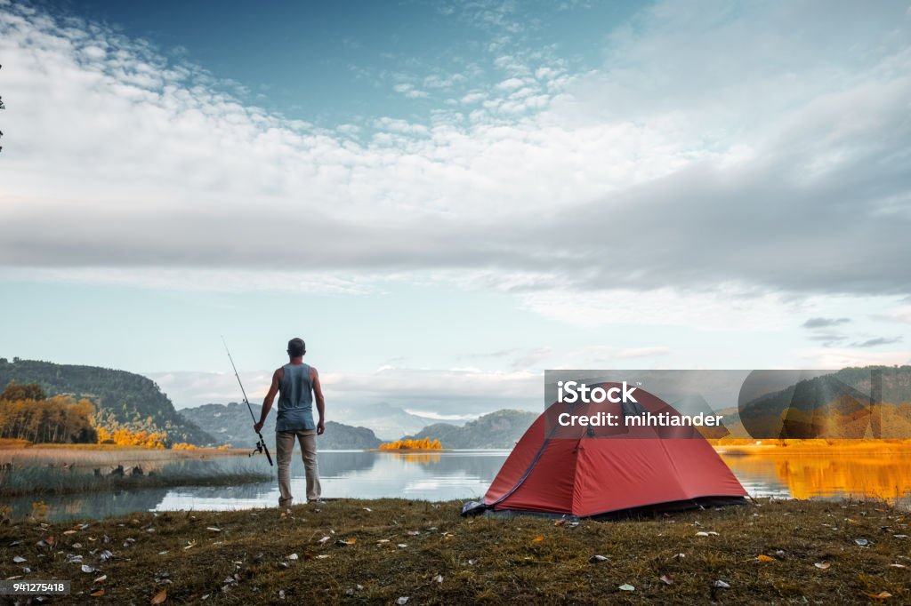 Angler stands on the coast of a lake Angler stands on the coast of a lake with fishing rod Camping Stock Photo