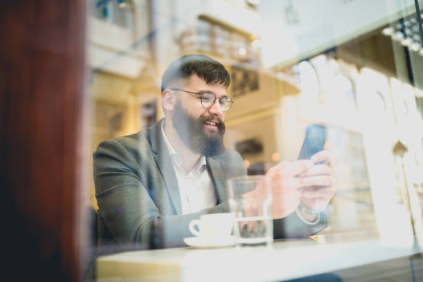 istock Businessman using phone, sitting in the window of cafe on coffee break 941275596