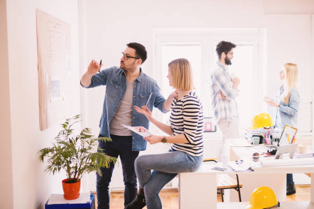 istock Young confident productive and creative business people preparing a plan for better results and statistics on the wall panel in the modern bright office. 941282758