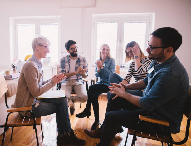istock Young addicted people having celebrating situation while sitting together on special group therapy. Brave persistent guy getting applause after his confession and progress. 941285166