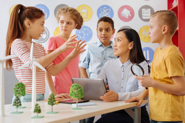 Smart schoolchildren sharing their ecology project idea with teacher Little geniuses. Pleasant smart schoolchildren sharing their ecology project idea with their teacher while she listening attentively to the group leader science class stock pictures, royalty-free photos & images