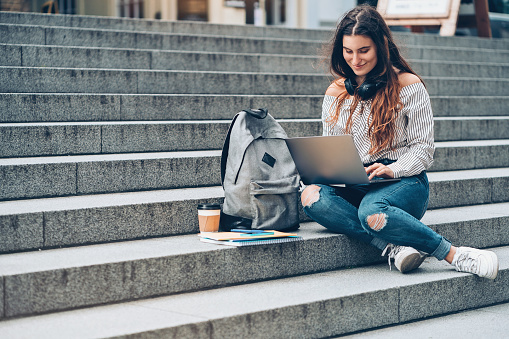 Student sitting on a staircase outdoors and using laptop