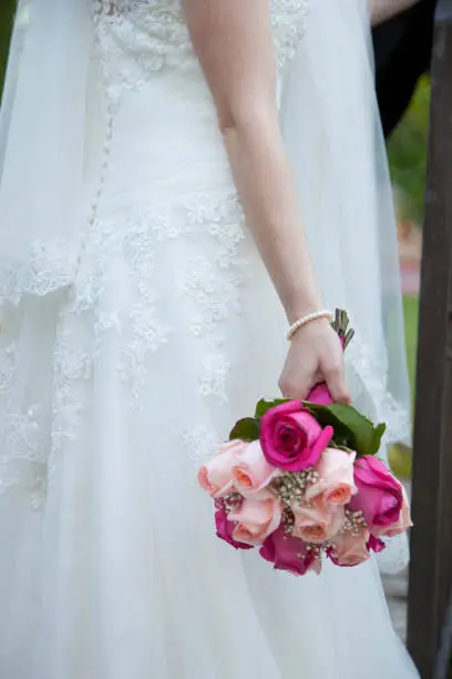 detail of the bridal bouquet in salmon and pink colors, which holds the bride placed on her back, wearing her white dress