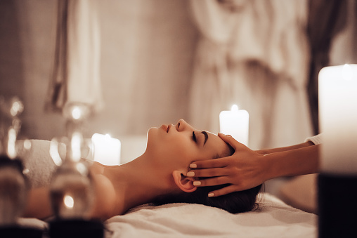 Attractive young woman is relaxing in spa and wellness center while receiving head massage. Beauty treatment concept.