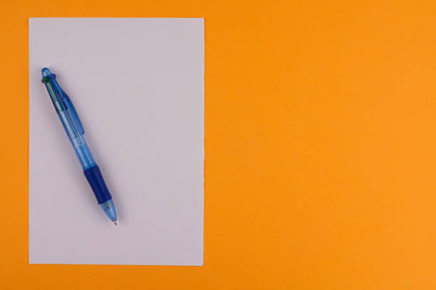 istock One multi color blue transparent ballpoint and white blank rectangle paper on background of orange paper with copy space 941312552