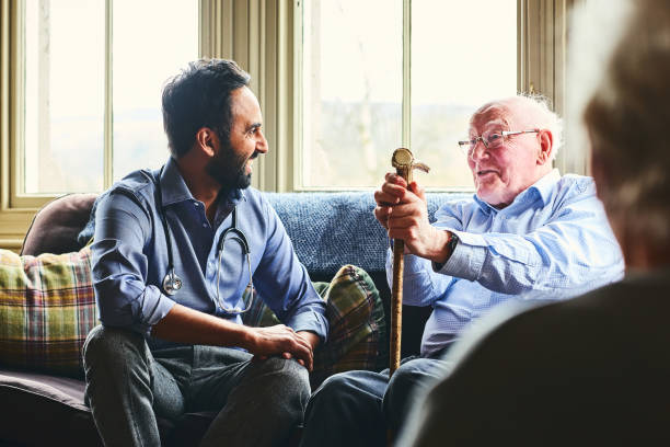 Smiling doctor visiting senior man at home Young male doctor and senior man sitting on sofa and smiling during home visit seniors talking stock pictures, royalty-free photos & images