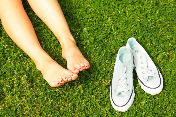 istock Female bare feet on mawed lawn grass. Young woman resting outdoors barefoot, take a break concept. Student on college campus yard. 941325672
