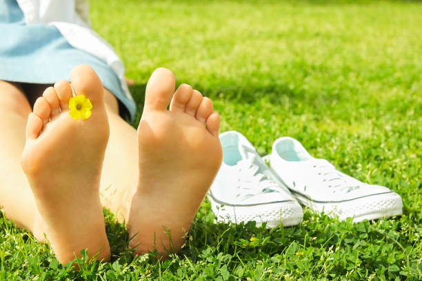 Close up of barefoot young woman bare feet sitting on juicy green grass lawn, toe flower. Smooth female legs outdoors sitting in park. Foot fungus & cracked heels cure concept. Background, copy space.