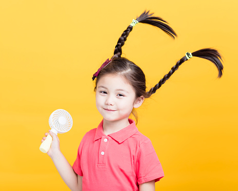 smiling little girl enjoying cool wind from electric fan