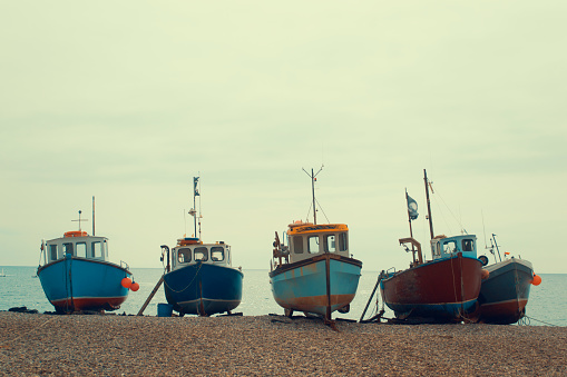 4 fishing boats lie on a pebble beach with the sea in the background, photographed in the Devon fishing village of Beer.