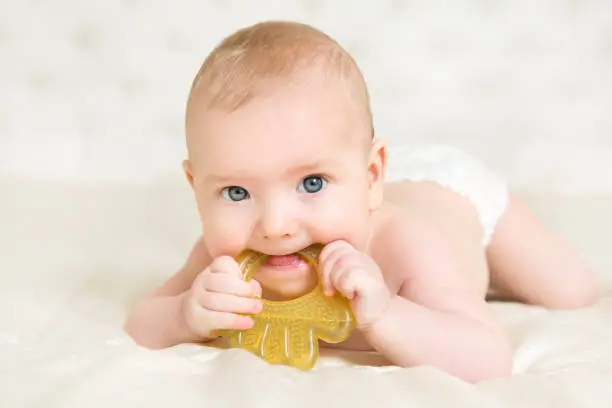 Baby Teether, Kid Bite Teething Toy in Mouth, Infant Child Growing First Tooth, Little Boy in Diapers Crawling on White blanket