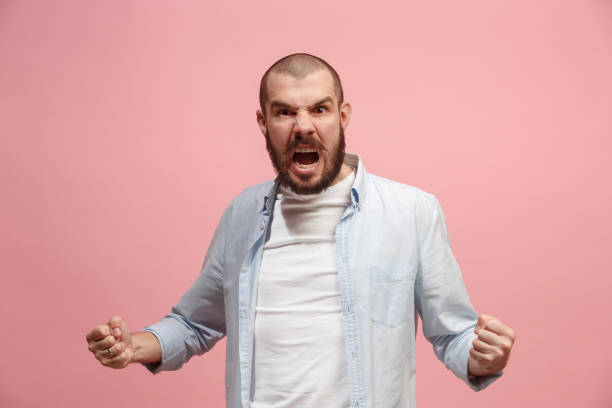 istock The young emotional angry man screaming on pink studio background 941373526