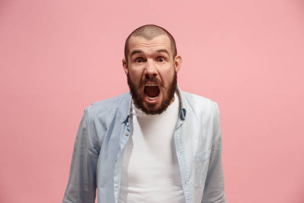 istock The young emotional angry man screaming on pink studio background 941373772
