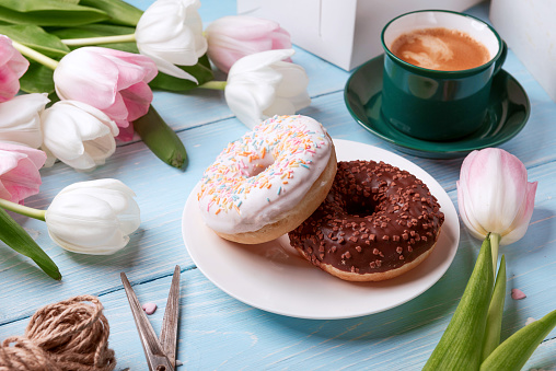 donuts, coffee and tulips on a blue wooden background. breakfast in summer with family.