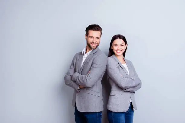 Photo of Concept of partnership in business. Young man and woman standing back-to-back with crossed hands against gray background