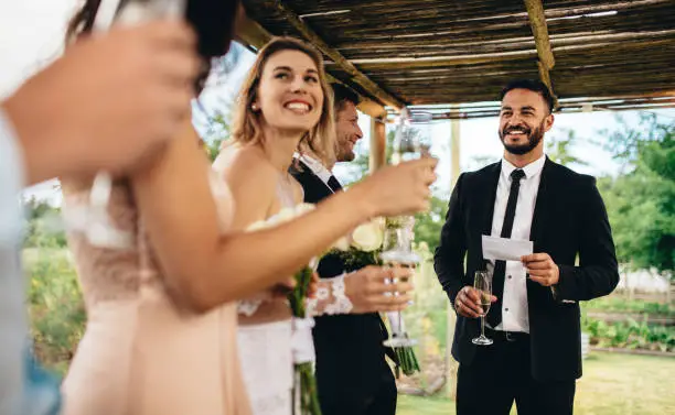 Best man performing speech for toast at wedding reception. Bride and groom listening to a speech at their wedding reception.