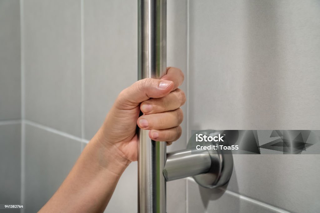 Woman holding on handrail in toilet. Security Bar Stock Photo