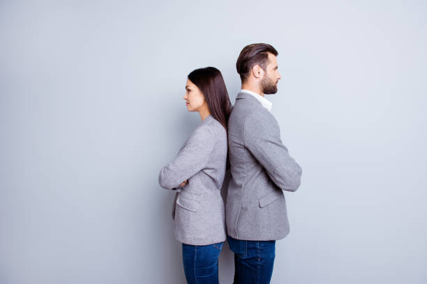 dos profesionales en negocios y finanzas en chaquetas gris y jeans de pie espalda con espalda sobre fondo gris - two people back to back businesswoman women fotografías e imágenes de stock