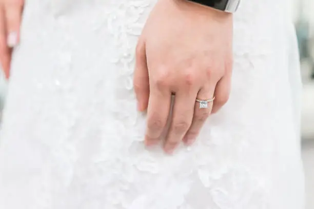 Closeup of princess cut diamond engagement ring on woman's female hand, white lace wedding dress, bracelet watch