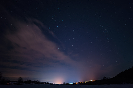 Starry sky with small clouds over the city in the distance