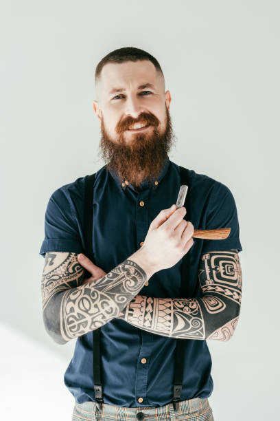 istock smiling tattooed man holding razor and looking at camera isolated on white 941404354