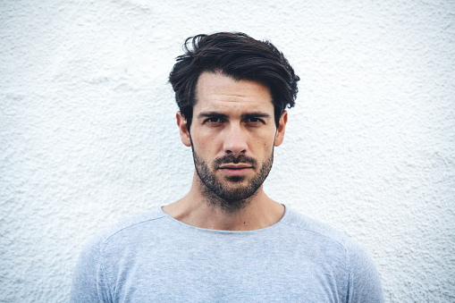 Portrait of a young man with black beard against white wall (Lleida, Catalonia, Spain).