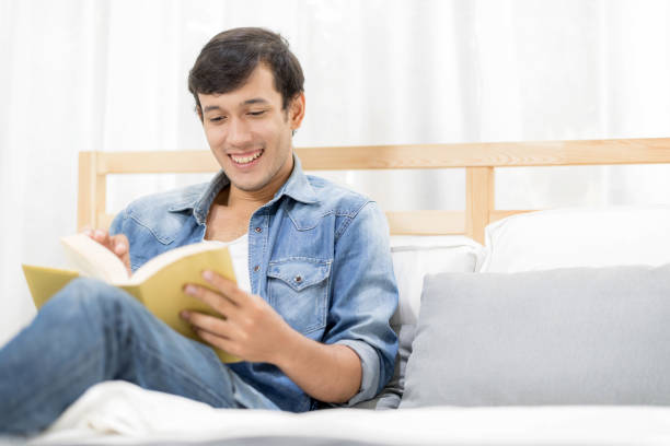 istock Handsome young man relaxing at home reading story for going online with using laptop computer on bed 941412926