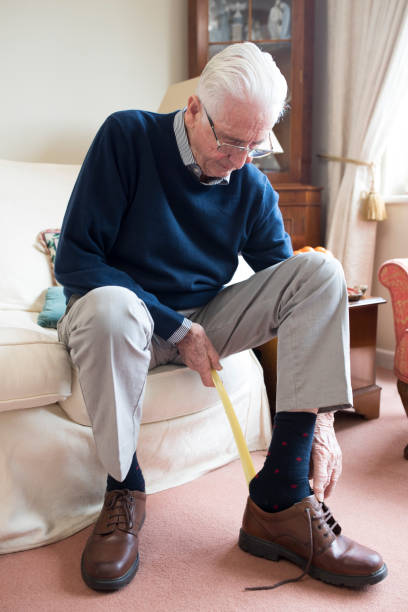 senior man using long handled shoe horn to put on shoes - calca imagens e fotografias de stock