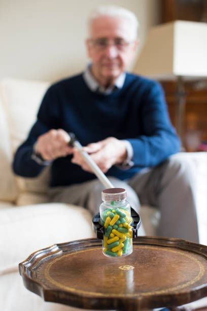 starszy mężczyzna za pomocą ramienia dotarcia do odbioru leków w domu - chwytak mechaniczny zdjęcia i obrazy z banku zdjęć