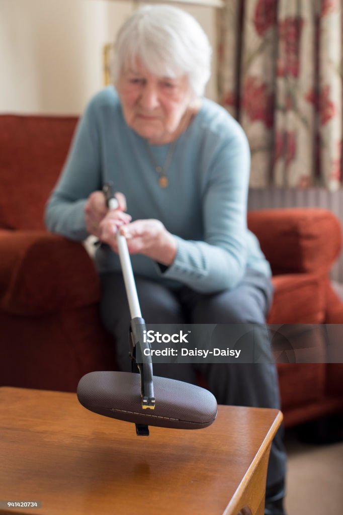 Senior Woman Using Reaching Arm To Pick Up Spectacles Case At Home Mechanical Grabber Stock Photo