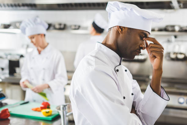 istock tired african american chef touching nose bridge at restaurant kitchen 941436310