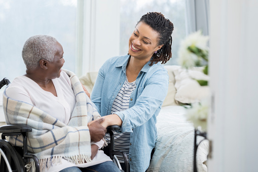 Mid adult woman helps her senior mother at home. The older woman is sitting in a wheelchair.