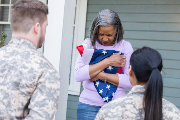 Upset mother grieves her soldier son's death African American senior mother holds a folded flag after receiving news of her soldier son's death. proud army mom stock pictures, royalty-free photos & images