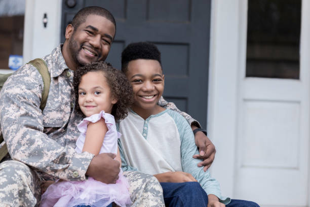 Happy reunion Happy military soldier is excited and relieved to be reunited with his preschool age daughter and preteen son. They are sitting on the front porch of their home. black military man stock pictures, royalty-free photos & images