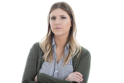 Uncertain young woman stands with arms crossed. She is looking at he the camera.