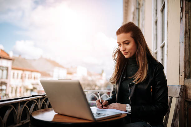 istock Young bussines woman working outdoors. Writting in a notebook while sitting in front of a laptop. 941440516