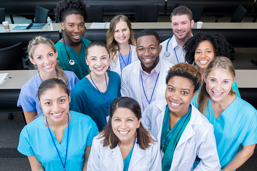 In this high angle view, a group of medical students stand in their classroom.  They look up and smile for the camera.
