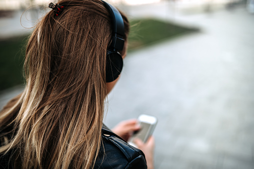 Rear view of a girl listening music on headphones outdoors.