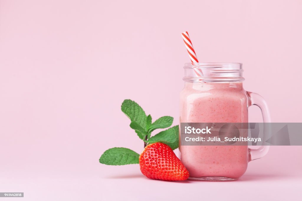 Strawberry smoothie or milkshake in mason jar decorated mint on pink table. Healthy food for breakfast and snack. Strawberry smoothie or milkshake in mason jar decorated mint on pink table. Healthy food for breakfast and snack. Punchy pastel. Smoothie Stock Photo