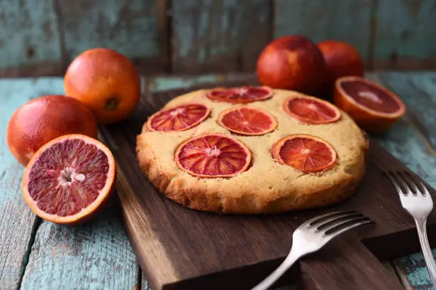 Homemade pastry. Traditional fruit cake with blood oranges on oak board on shabby blue background closeup