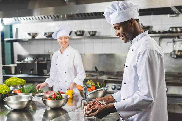 sourire de chef africain-américain tenant un plateau avec la viande crue à la cuisine du restaurant - chef restaurant cooking african descent photos et images de collection