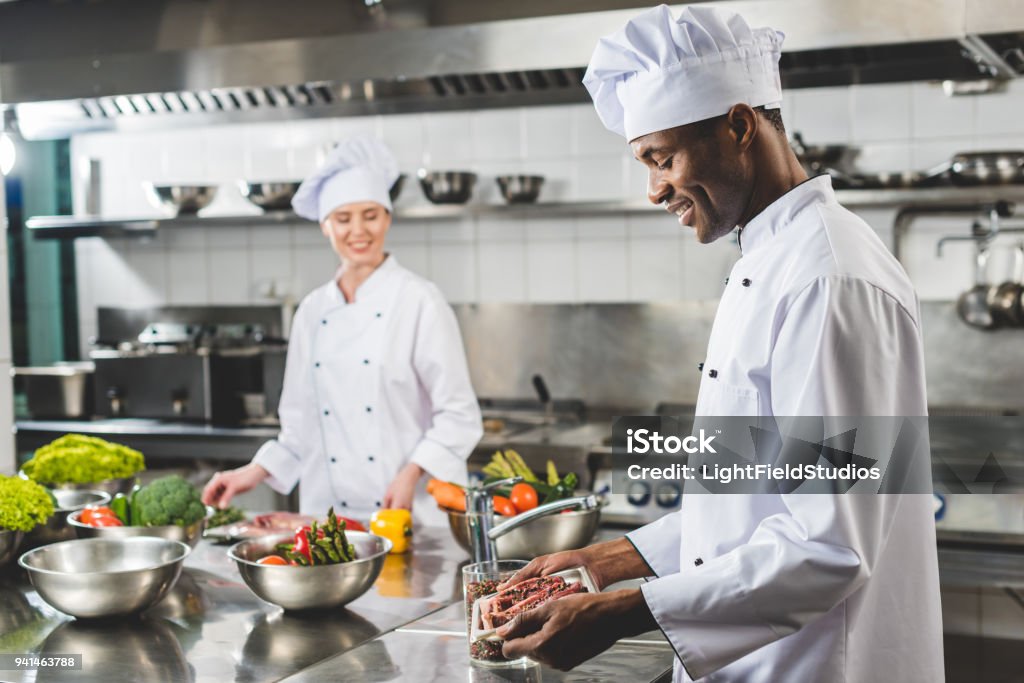 smiling african american chef holding tray with raw meat at restaurant kitchen Chef Stock Photo