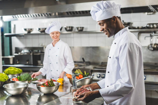 uśmiechnięty afroamerykański szef kuchni trzymający tacę z surowym mięsem w kuchni restauracyjnej - chef restaurant cooking african descent zdjęcia i obrazy z banku zdjęć