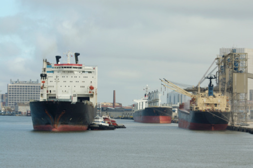 Cargo ships being moved by tugboats and unloading at dock in busy commercial port. Galveston,TX